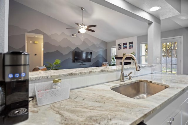 kitchen with light stone countertops, vaulted ceiling, ceiling fan, sink, and white cabinets