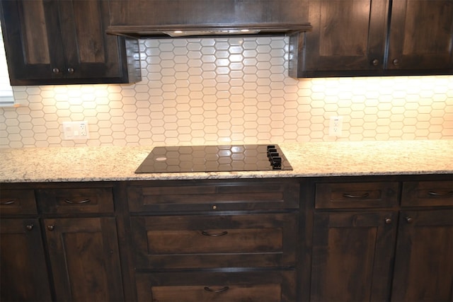 kitchen with tasteful backsplash, light stone countertops, black electric stovetop, and custom range hood