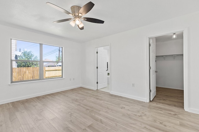 unfurnished bedroom with ceiling fan, ensuite bathroom, light hardwood / wood-style floors, a walk in closet, and a closet