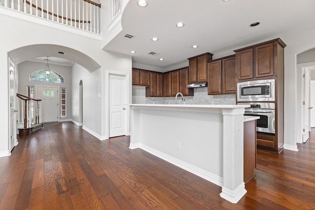 kitchen with a kitchen island with sink, sink, appliances with stainless steel finishes, tasteful backsplash, and dark hardwood / wood-style flooring