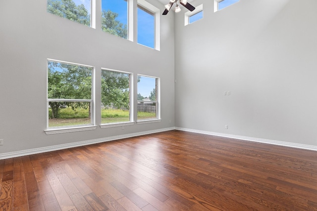 unfurnished living room with a high ceiling, dark hardwood / wood-style floors, a wealth of natural light, and ceiling fan