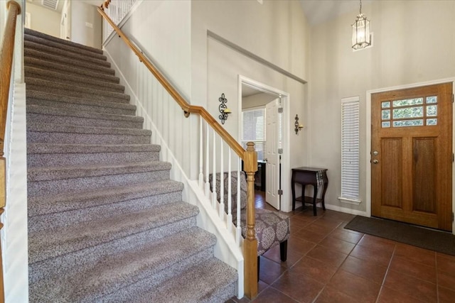 foyer entrance with baseboards, dark tile patterned floors, a high ceiling, and stairs