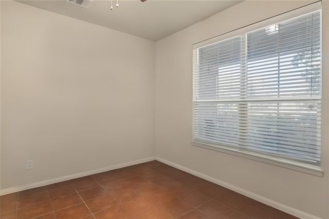 tiled spare room with visible vents, ceiling fan, and baseboards