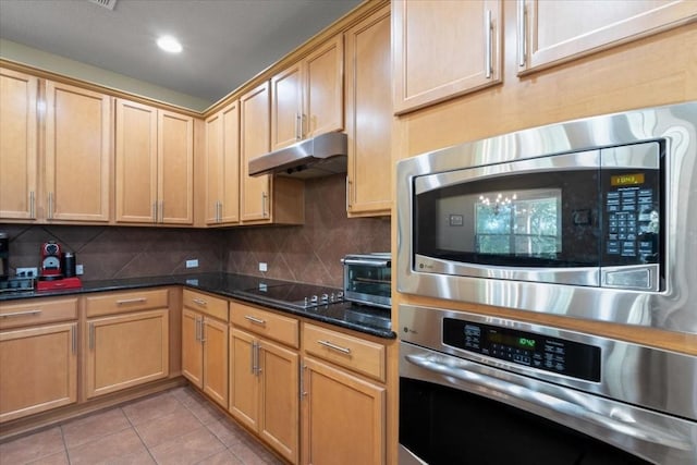 kitchen with light tile patterned floors, decorative backsplash, dark stone countertops, stainless steel appliances, and under cabinet range hood