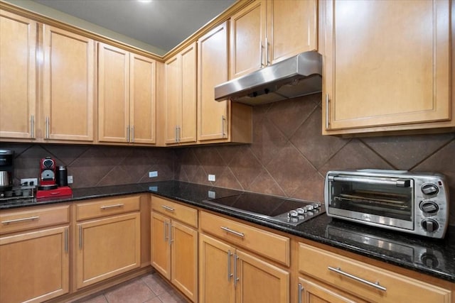 kitchen with dark stone counters, a toaster, backsplash, and under cabinet range hood