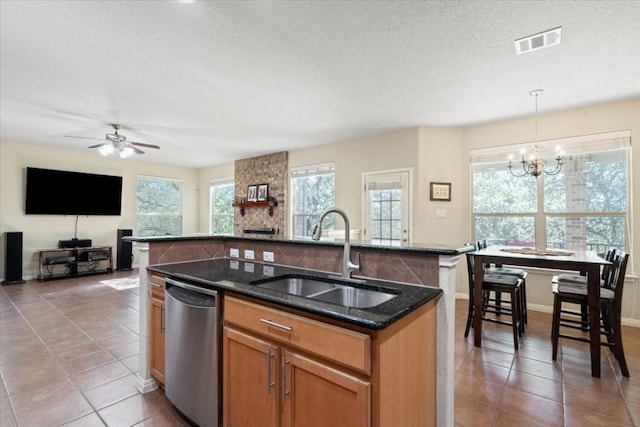 kitchen featuring visible vents, dishwasher, hanging light fixtures, a kitchen island with sink, and a sink