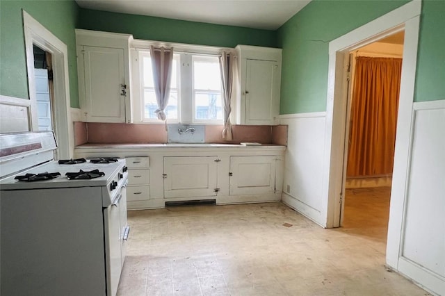 kitchen with white gas range, white cabinetry, and sink