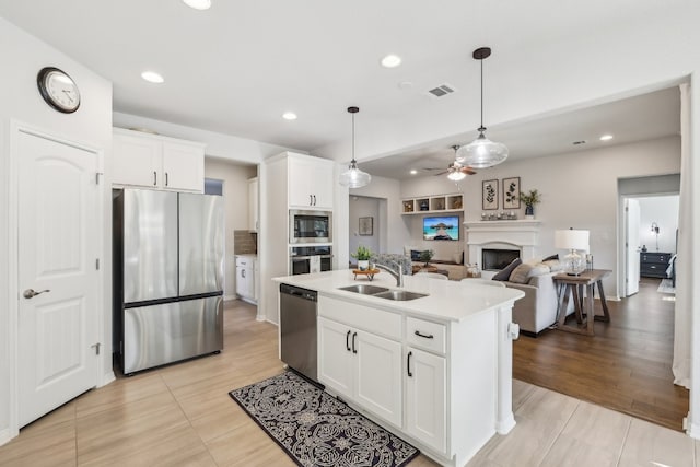 kitchen with appliances with stainless steel finishes, ceiling fan, a kitchen island with sink, sink, and white cabinetry