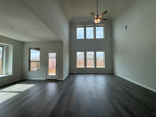 unfurnished living room featuring dark wood-type flooring, a wealth of natural light, ceiling fan, and a towering ceiling