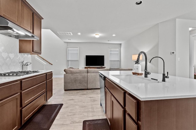 kitchen featuring backsplash, stainless steel appliances, exhaust hood, sink, and a center island with sink