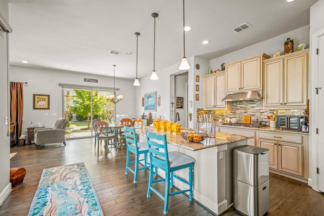 kitchen featuring pendant lighting, backsplash, a kitchen breakfast bar, light stone counters, and a center island with sink