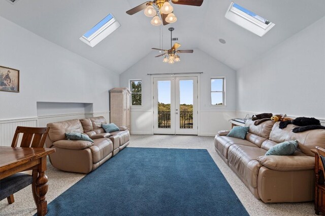 carpeted living room featuring ceiling fan, wood walls, lofted ceiling with skylight, and french doors