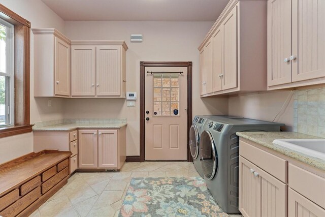 clothes washing area with washer and dryer, cabinets, light tile patterned floors, and sink