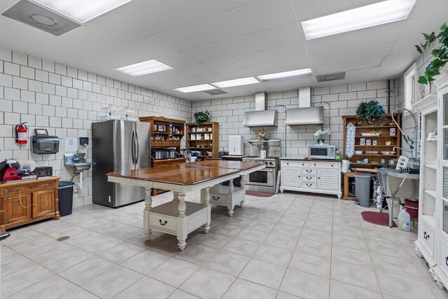 kitchen featuring a breakfast bar, wall chimney exhaust hood, a kitchen island, white cabinetry, and stainless steel refrigerator