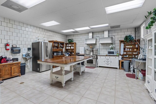 1092 Fm 3000, Elgin, TX 78621 - kitchen featuring stainless steel appliances, tile walls, wall chimney exhaust hood, light tile patterned floors, and a drop ceiling