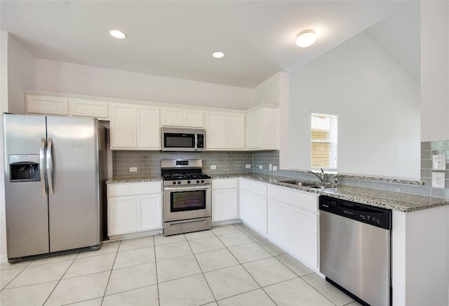 kitchen with white cabinets, sink, vaulted ceiling, light stone countertops, and stainless steel appliances