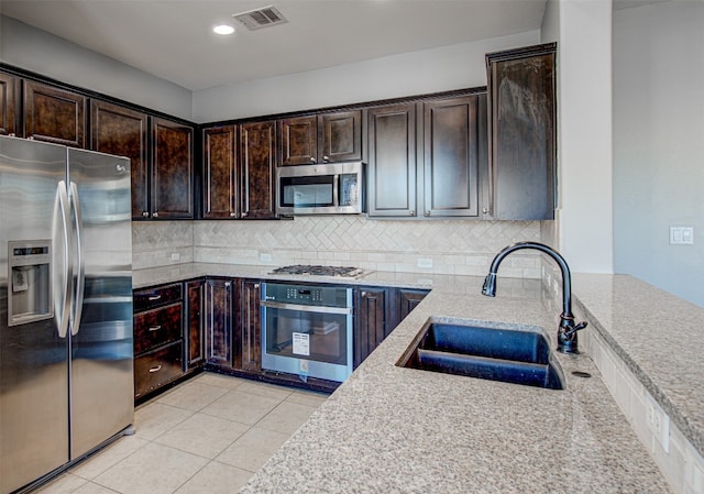 kitchen featuring light stone countertops, appliances with stainless steel finishes, tasteful backsplash, dark brown cabinets, and sink