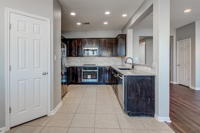 kitchen with dark brown cabinetry, light stone countertops, sink, stainless steel appliances, and light wood-type flooring