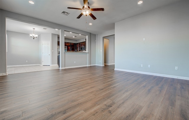 unfurnished living room featuring ceiling fan with notable chandelier and light wood-type flooring