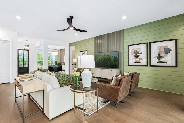 living room featuring wood-type flooring, ceiling fan with notable chandelier, and wood walls