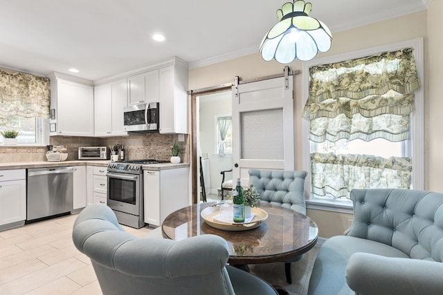 kitchen featuring a barn door, backsplash, stainless steel appliances, ornamental molding, and white cabinets