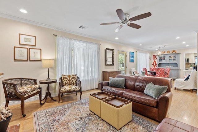 living room with ceiling fan with notable chandelier, light hardwood / wood-style flooring, and crown molding