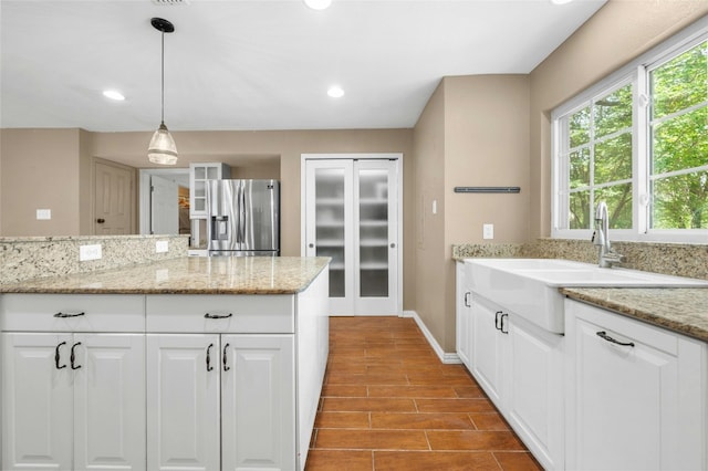 kitchen featuring light stone countertops, sink, hanging light fixtures, light hardwood / wood-style flooring, and stainless steel fridge