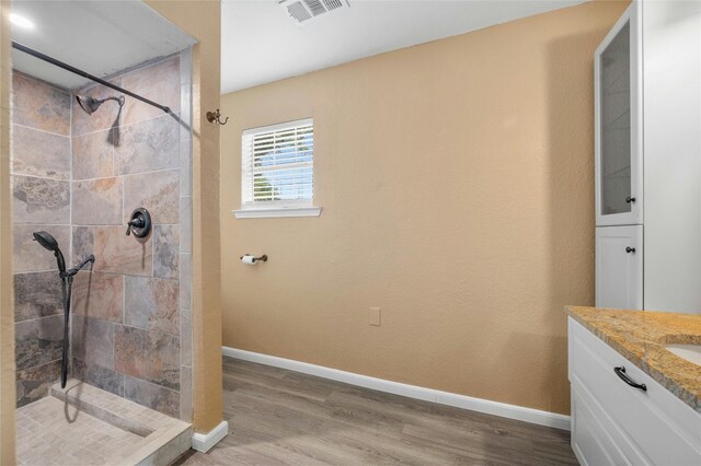 bathroom with hardwood / wood-style floors, vanity, and a tile shower