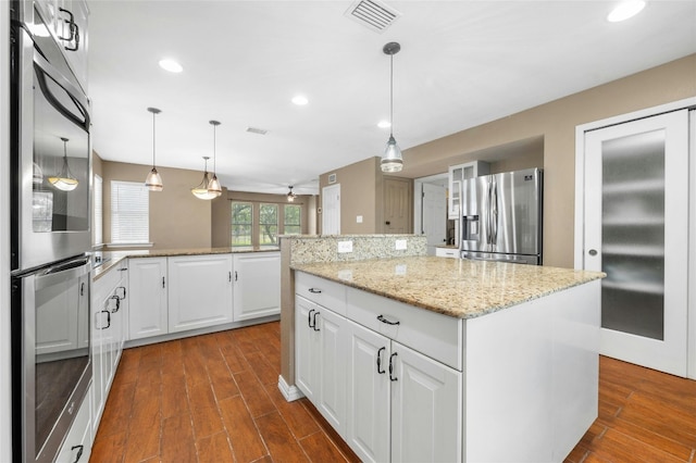 kitchen featuring a center island, dark wood-type flooring, white cabinets, appliances with stainless steel finishes, and decorative light fixtures