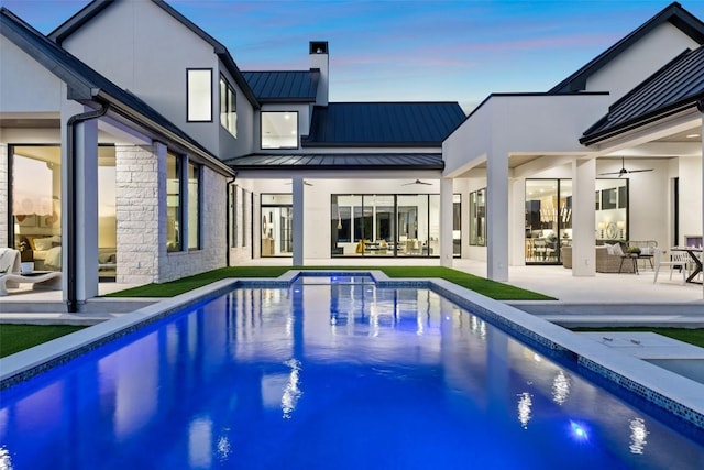 pool at dusk with a patio area and ceiling fan