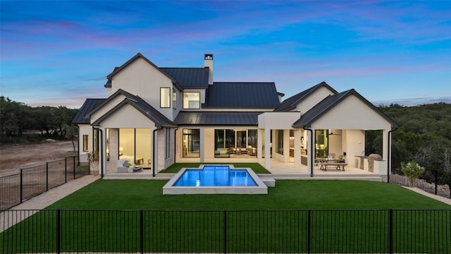 back house at dusk featuring outdoor lounge area, a patio area, a fenced in pool, and a yard