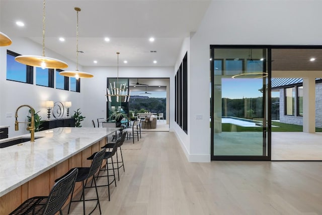 kitchen with light stone countertops, sink, light hardwood / wood-style flooring, pendant lighting, and a breakfast bar