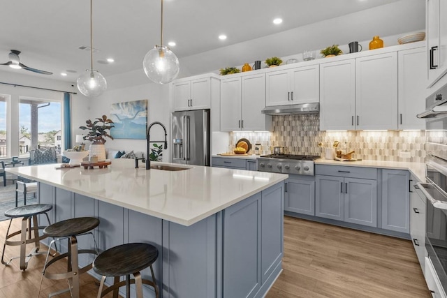 kitchen with a kitchen island with sink, hanging light fixtures, sink, light hardwood / wood-style flooring, and stainless steel appliances