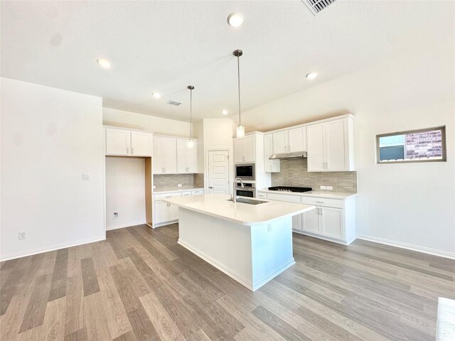 kitchen with decorative light fixtures, a kitchen island with sink, sink, and white cabinetry