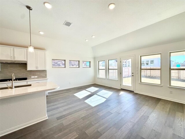 kitchen featuring lofted ceiling, pendant lighting, decorative backsplash, white cabinetry, and light stone counters