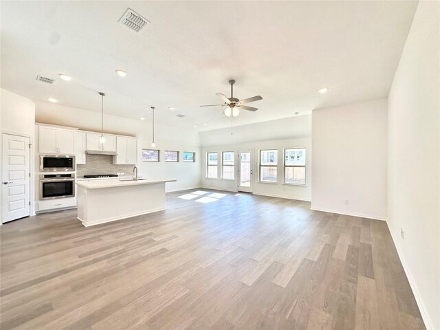 kitchen featuring appliances with stainless steel finishes, decorative light fixtures, white cabinetry, an island with sink, and light wood-type flooring