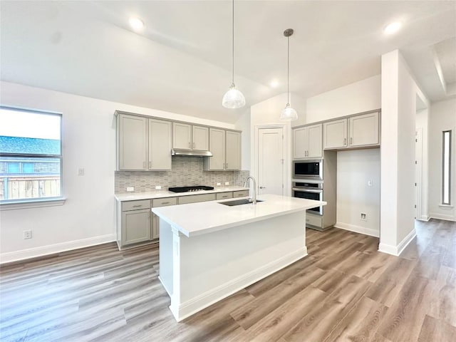 kitchen with a center island with sink, hanging light fixtures, stainless steel appliances, sink, and tasteful backsplash