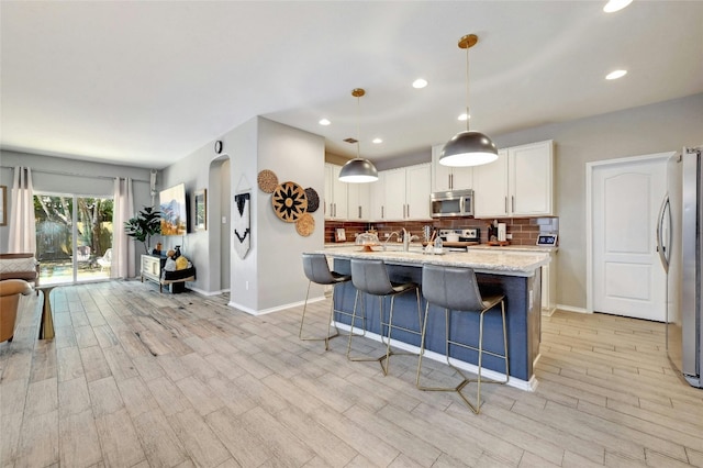 kitchen with backsplash, light hardwood / wood-style floors, pendant lighting, and appliances with stainless steel finishes