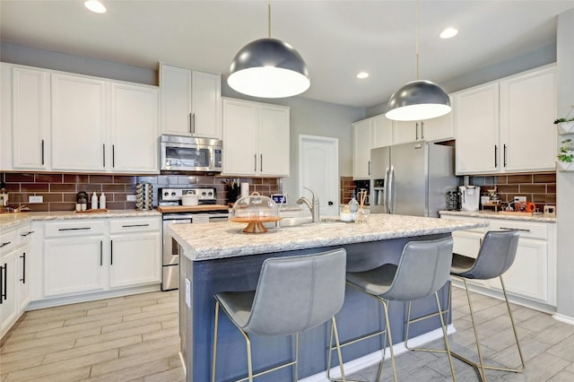 kitchen with decorative backsplash, an island with sink, appliances with stainless steel finishes, decorative light fixtures, and white cabinetry