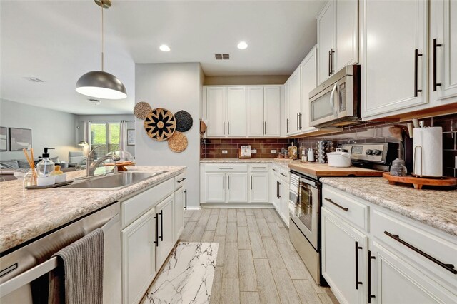 kitchen featuring white cabinetry, sink, hanging light fixtures, and appliances with stainless steel finishes