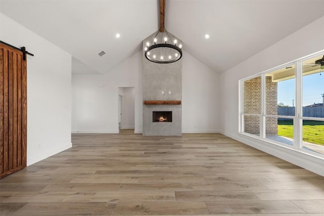 unfurnished living room with a large fireplace, a barn door, light hardwood / wood-style flooring, and high vaulted ceiling