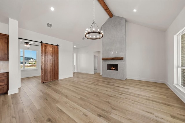 unfurnished living room featuring beam ceiling, a barn door, a fireplace, and light wood-type flooring