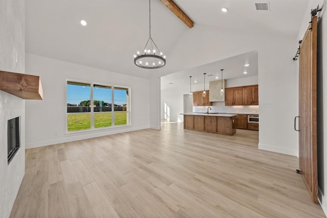 unfurnished living room with sink, beam ceiling, a barn door, a notable chandelier, and light hardwood / wood-style floors