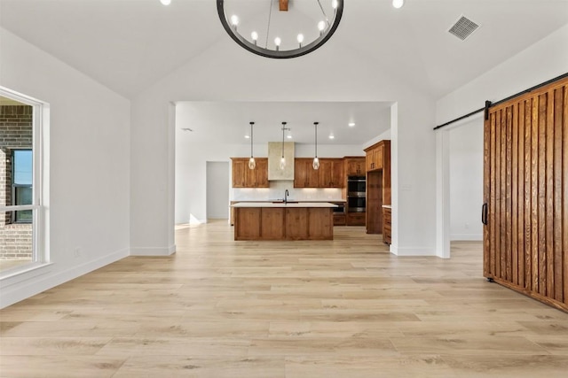 kitchen featuring a barn door, pendant lighting, vaulted ceiling, light hardwood / wood-style floors, and a center island with sink