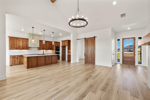 kitchen with pendant lighting, a center island with sink, a barn door, light hardwood / wood-style floors, and a chandelier