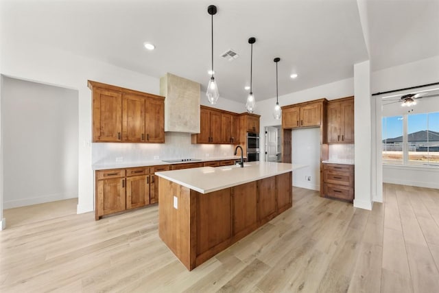 kitchen with ceiling fan, pendant lighting, light hardwood / wood-style floors, black electric cooktop, and a center island with sink