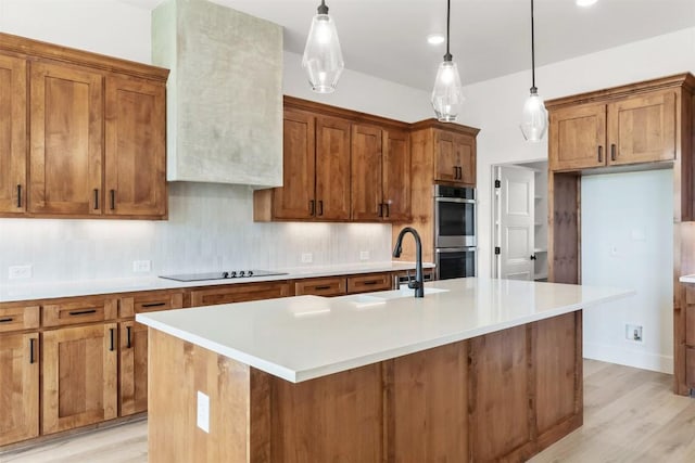 kitchen with a center island with sink, pendant lighting, light wood-type flooring, and double oven