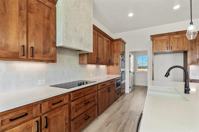 kitchen featuring black electric stovetop, sink, light hardwood / wood-style flooring, double oven, and decorative light fixtures