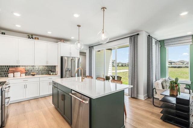 kitchen with sink, white cabinetry, decorative light fixtures, appliances with stainless steel finishes, and an island with sink