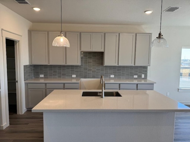 kitchen with gray cabinets, sink, backsplash, hanging light fixtures, and dark wood-type flooring